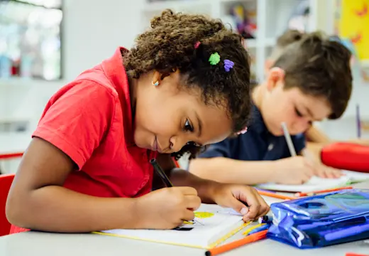 Young girl writing in a class with her pencil case in front of her