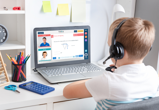 A child sits at a desktop with a laptop open in front of him. On the screen a smart learning tool can be seen with a tutor on screen supporting the child.