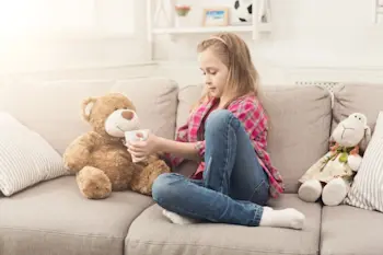 beautiful little girl on a sofa treating her teddy bear with tea
